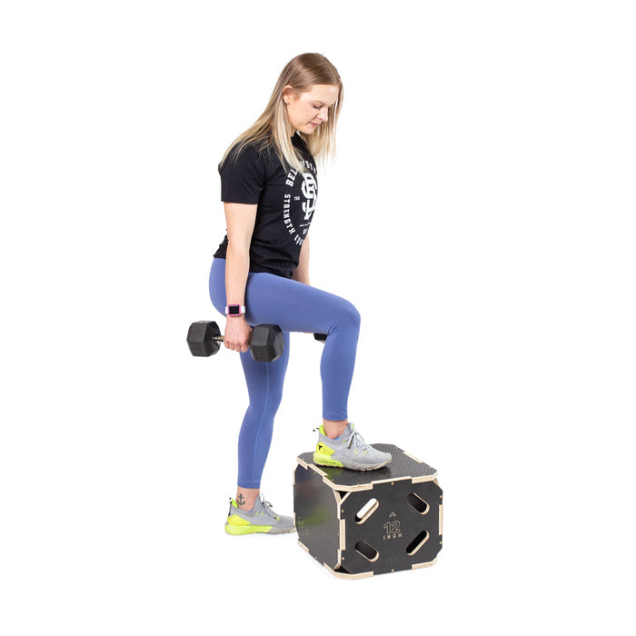 A woman in workout clothes uses the Bells of Steel 3 in 1 Anti-Slip Wood Plyo Boxes, stepping up with a dumbbell on a black box against a white background—ideal for home gym workouts.