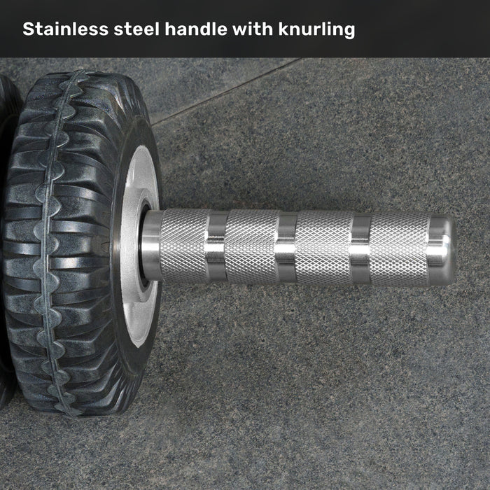 Close-up of the ABsyidyan Stainless Steel Ab Roller by Bells of Steel USA, featuring a knurled stainless steel handle and extra-wide dual wheels on a textured gray surface. Text above: "Stainless steel handle with knurling.