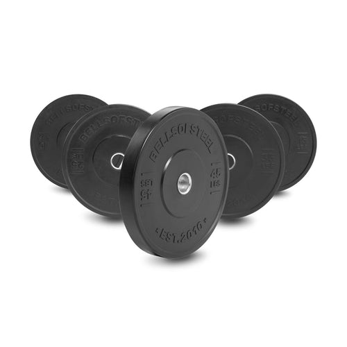 Five All-Black Bumper Plates by Bells of Steel are arranged upright in a semicircle, largest at the front. Each plate displays weight markings, the Bells of Steel logo, and features a durable stainless steel insert ring.