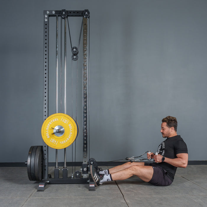 A man in athletic clothing sits on the floor using Bells of Steel USA Aluminum Handles Pair with Bearings, pulling them toward his torso. A large yellow weight plate is mounted on the accessory against a gray wall background.