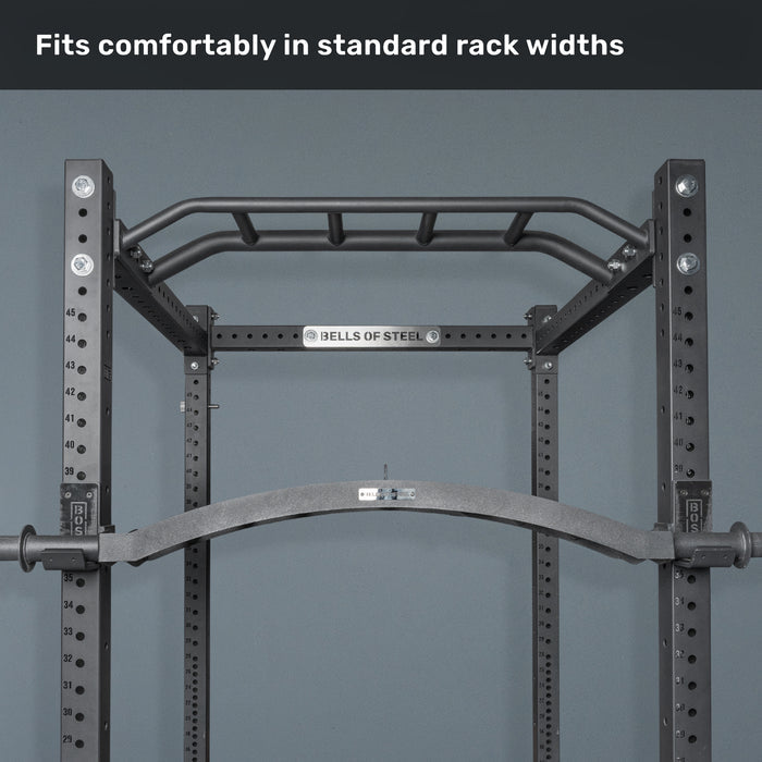A pull-up bar attachment mounted on a black Bells of Steel power rack against a gray wall, with "Fits comfortably in standard rack widths" at the top—ideal with cable attachments or specialty bars like the Arch Nemesis Swiss Bar.