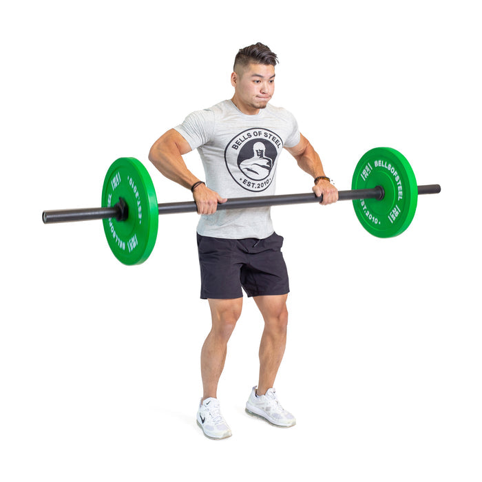 A man lifts a Bells of Steel Axle Bar with green plates to chest height, performing an upright row in a gray t-shirt and black shorts against a white background—perfect for building grip strength and strongman training.