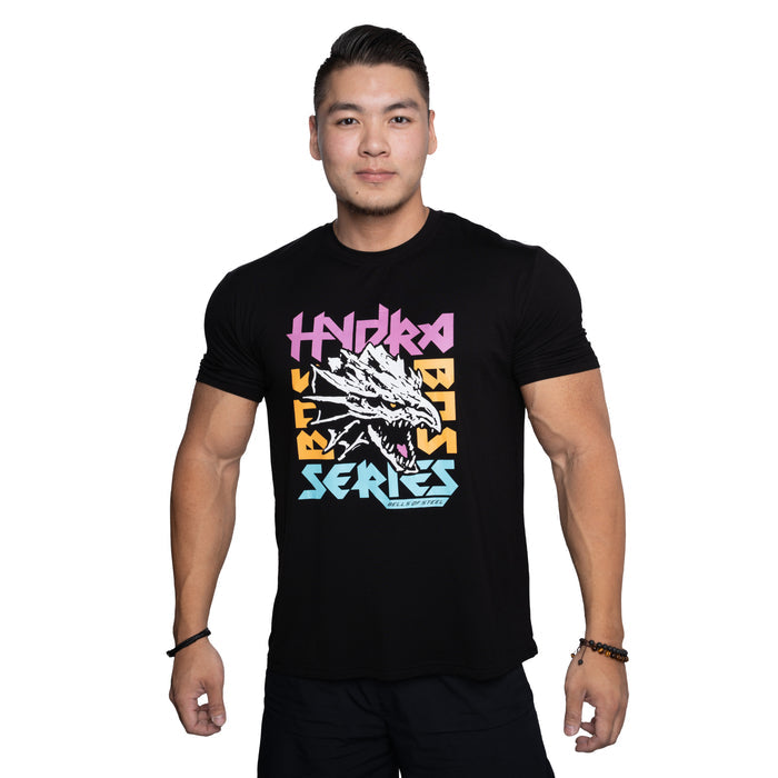 A man with short dark hair wears the Bells of Steel Bamboo T-Shirt, featuring a stylized dragon head and colorful "HYDRA BEAST SERIES" text, as he stands confidently against a white background.