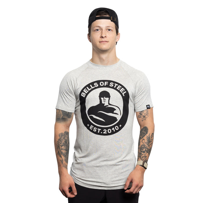A person in a backward black cap and a light gray Bells of Steel Bamboo T-Shirt stands facing forward, displaying tattooed arms against a plain white background.