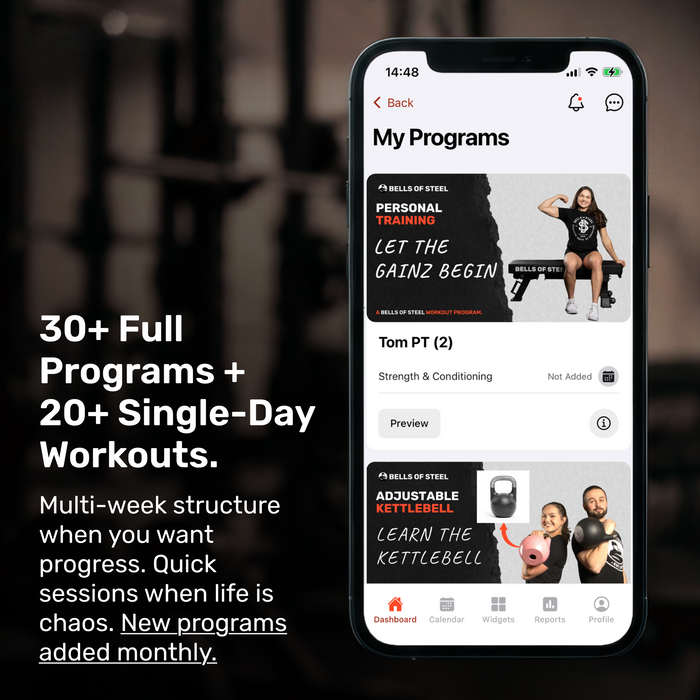 A smartphone displays the Bells of Steel Training App by Bells of Steel, showcasing “30+ Full Programs + 20+ Single-Day Workouts” and “New programs added monthly,” against a blurred gym background.