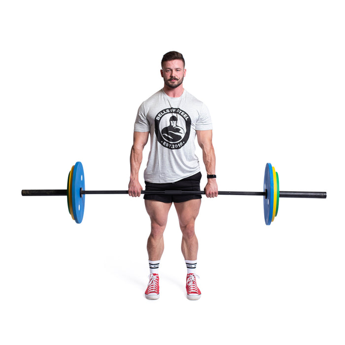 A man in a gray T-shirt and black shorts holds a barbell with Bells of Steel Calibrated Powerlifting Plates - KG, standing against a white background. He's wearing red sneakers and white socks.