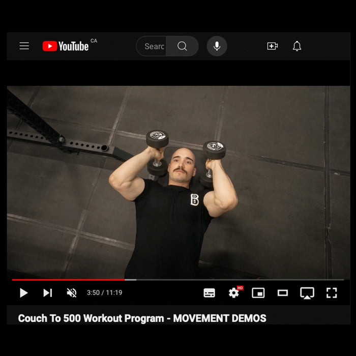 A man does a chest press with dumbbells on a gym floor. The "Couch to 500kg - Workout Program" by Bells of Steel is a great digital program for beginners starting strength training or a 12-week fitness journey.