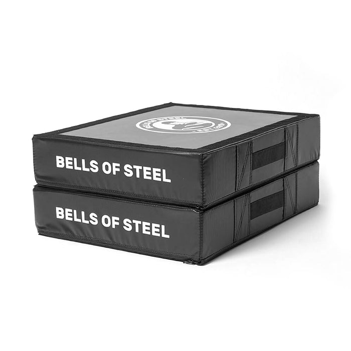 A pair of black Bells of Steel Deadlift Pads, each with reinforced stitching, side handles, and white "BELLS OF STEEL" text—perfect silencer pads to reduce weightlifting noise.
