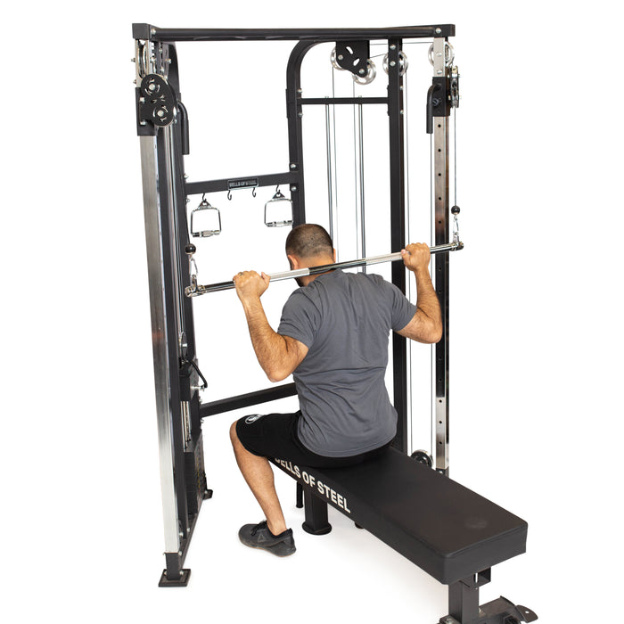 Wearing a gray shirt and black shorts, a person sits on a bench performing a lat pulldown by pulling the Bells of Steel Double Hook Straight Bar Cable Attachment behind their neck.