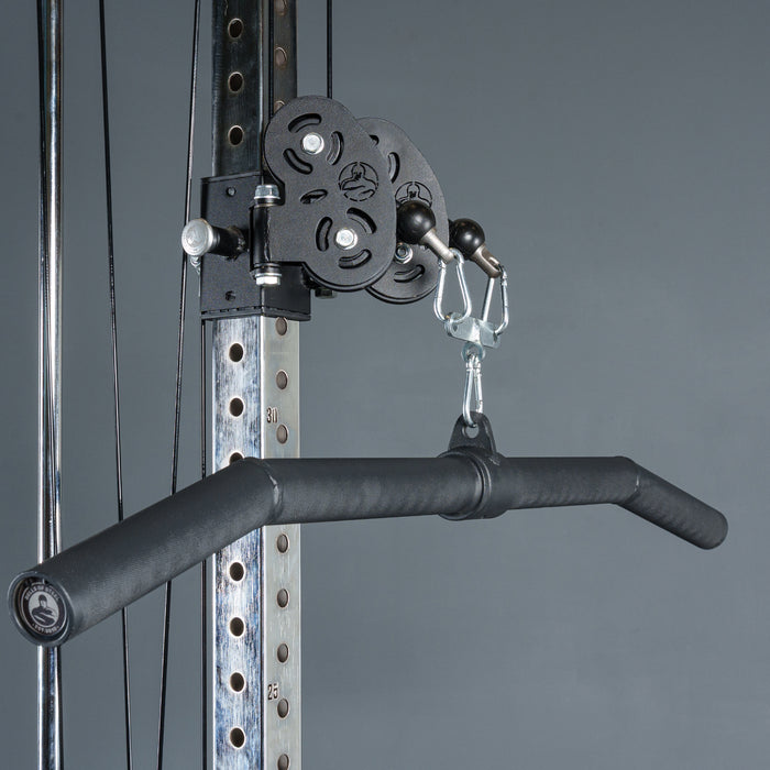 A close-up of the Bells of Steel Fat Bar - Lat Pulldown Bar with a wide-grip attachment on a cable machine. Its metal frame, set against a gray background, features numbered holes for adjustable height—perfect for grip strength training.