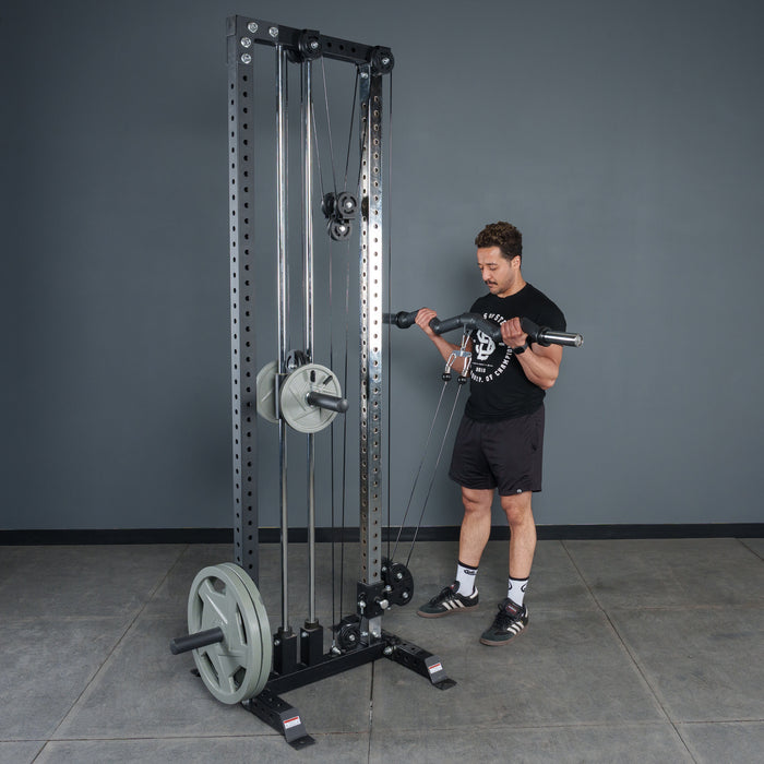 In a gym with gray walls and a concrete floor, a man in athletic clothing uses the Bells of Steel Fat Bar - Olympic Curl Bar Cable Attachment for bicep curls, boosting grip strength during his workout.