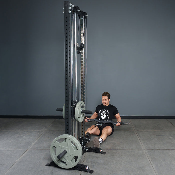 A man sits on the gym floor using the Bells of Steel Fat Bar - Olympic Curl Bar Cable Attachment for seated rows. Wearing a black T-shirt and gym shoes, he pulls the handlebar to his torso to build grip strength.