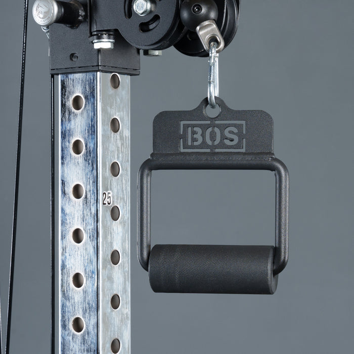 Close-up of a metallic gym cable machine with a Fat Bar - Single D Handle by Bells of Steel hanging from a hook. This handle boosts grip strength, and the vertical post has numbered holes for adjustable height settings.