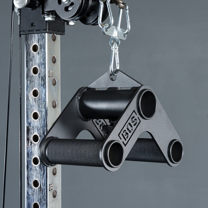 A close-up of the Bells of Steel Fat Bar - T-Bar Row Cable Attachment, featuring a black triangular metal design for enhanced grip strength, hangs from a carabiner on a cable machine against a plain gray background.