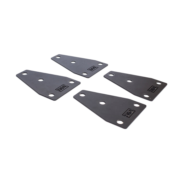 Four black metal plates with rounded edges and four holes each, featuring a small "JKS" logo, are displayed against a white background. They are compatible with Manticore power racks for enhanced stability. Product: Manticore Flat Foot Components by Bells of Steel.
