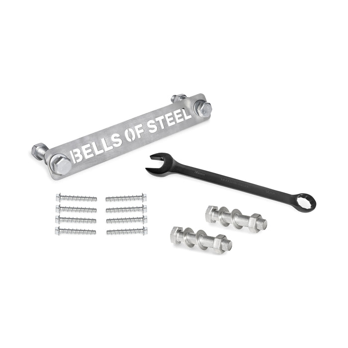 Manticore Hardware by Bells of Steel—including a metal bar, black wrench, bolts, nuts, screws, and concrete anchor bolts—is neatly arranged on a white surface, ready for power rack assembly.