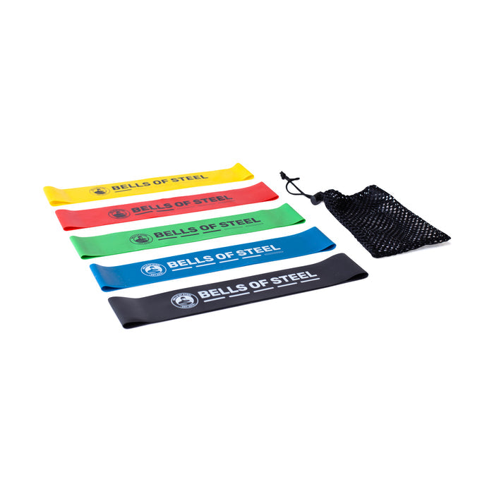 Five Bells of Steel Mini Bands in yellow, red, green, blue, and black are arranged beside a black mesh pouch on a white background. These versatile resistance bands are ideal gym accessories for any workout.