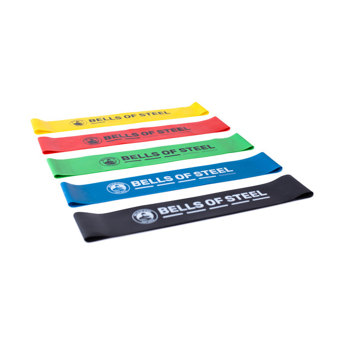 Five Bells of Steel Mini Bands in yellow, red, green, blue, and black are arranged diagonally on a white background—essential gym accessories for versatile resistance training.