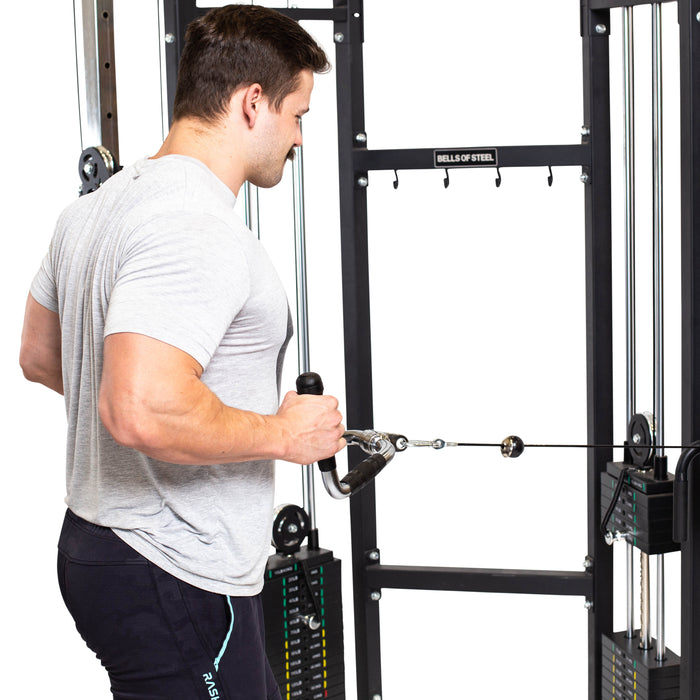 A man in a gray t-shirt uses the Bells of Steel Multi Purpose Close Grip Cable Attachment on a cable machine, pulling the handle toward his torso during a row exercise.