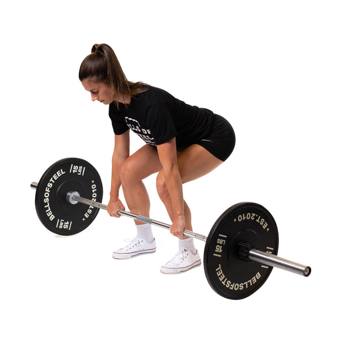 A person in black attire and white sneakers prepares to lift a Bells of Steel Olympic Weightlifting Barbell, demonstrating a deadlift starting position against a white background.