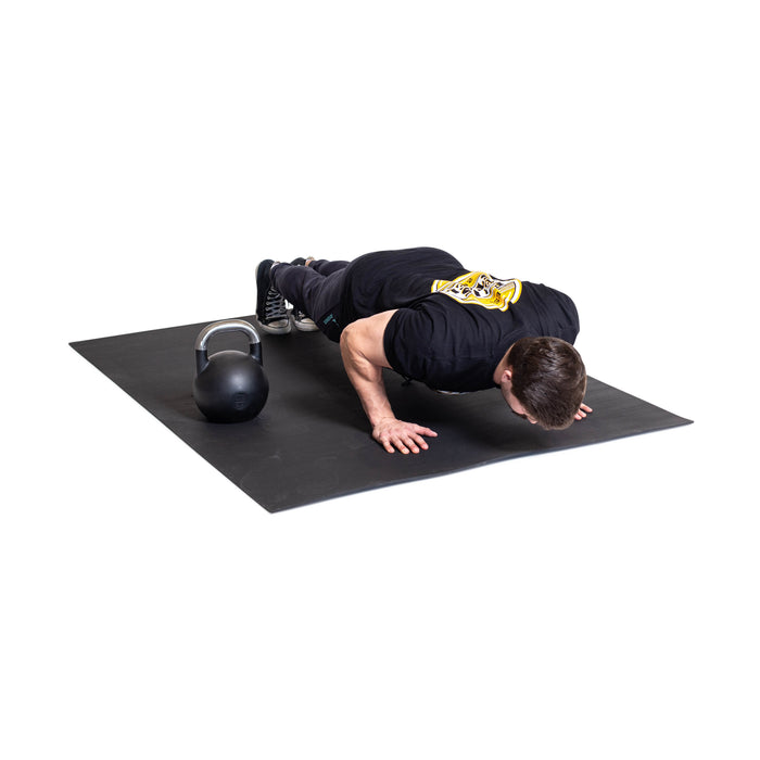 A man in a black T-shirt and pants does a push-up on the Bells of Steel Premium Rubber Flooring 4' x 6', with a kettlebell resting nearby on the left.