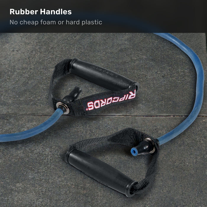 A blue Ripcords Premium Resistance Band by Bells of Steel USA, featuring black rubber handles and a visible “RIPCORDS” label, rests on a dark stone surface. The headline reads: “Rubber Handles - No cheap foam or hard plastic.” Ideal for workouts, these resistance bands are also fully compatible with any door anchor, offering versatile training options.