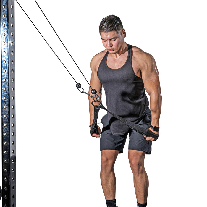 A man in a black tank top and shorts performs a triceps pushdown on a cable machine, gripping the Bells of Steel RocIT Tricep Strap with focus as he extends his arms downward.