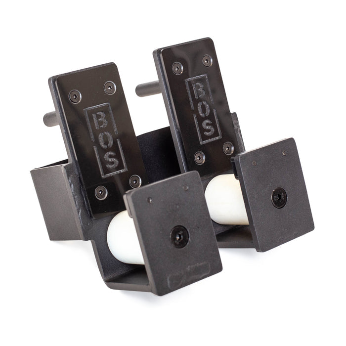 Two black rectangular Bells of Steel Roller J-Cups with sturdy nylon rollers hold white balls side by side on a white background—essential bench press accessories for your gym.