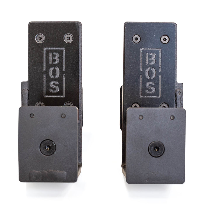 Two black metal Bells of Steel Roller J-Cups with "BOS" engraving are shown upright on a white background. Each features front screws and durable nylon rollers, ideal for bench press setups.