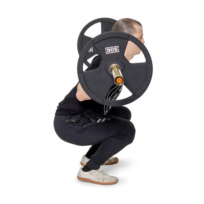 A person is doing a back squat with a barbell using Bells of Steel Rubber Coated Iron Weight Plates, dressed in black athletic wear and white shoes against a white background.