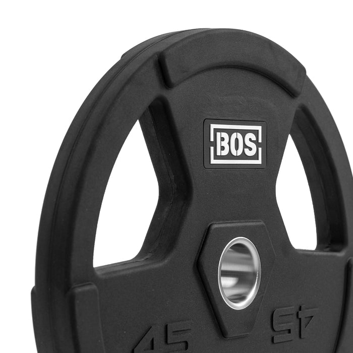 A close-up of a black Rubber Coated Iron Weight Plate by Bells of Steel shows "BOS" printed on it. It has a central mounting hole, ergonomic handles with cut-out grips, and is coated in durable virgin rubber for easy handling.