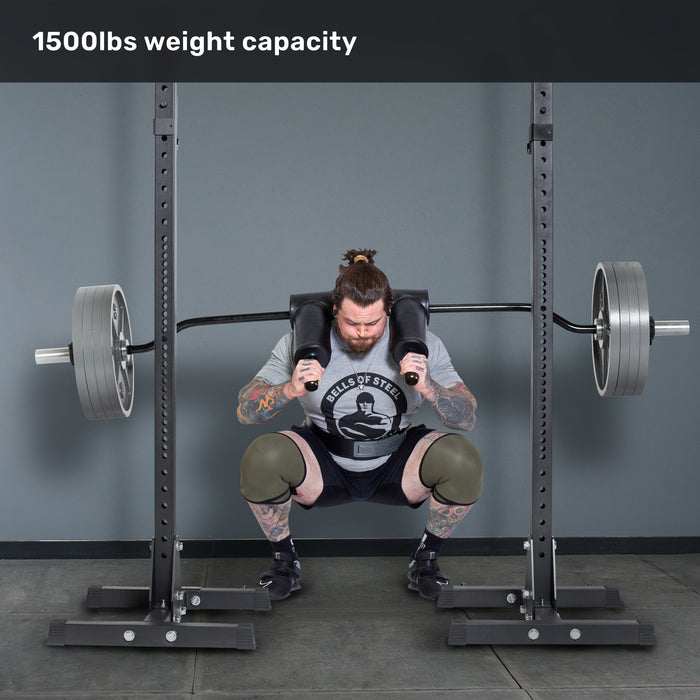 A tattooed man performs barbell squats on leg day using the Bells of Steel Safety Squat Bar - The SS4 in a gym rack, lifting a heavily loaded bar with "1500lbs weight capacity" displayed above.