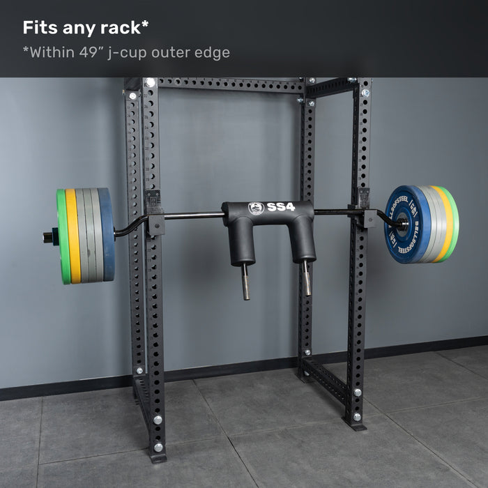 A Bells of Steel Safety Squat Bar - The SS4 is racked on a power rack in a gym with gray floors and walls. Text above: “Fits any rack* *Within 49” j-cup outer edge.” Perfect for your next leg day session.
