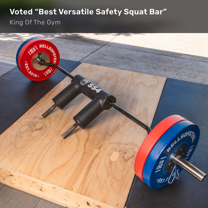 The Bells of Steel Safety Squat Bar - The SS4, with padded shoulder rests and colorful plates, sits on a wooden lifting platform outdoors—ideal for leg day. Text above: “Voted ‘Best Versatile Safety Squat Bar’ — King Of The Gym.”.