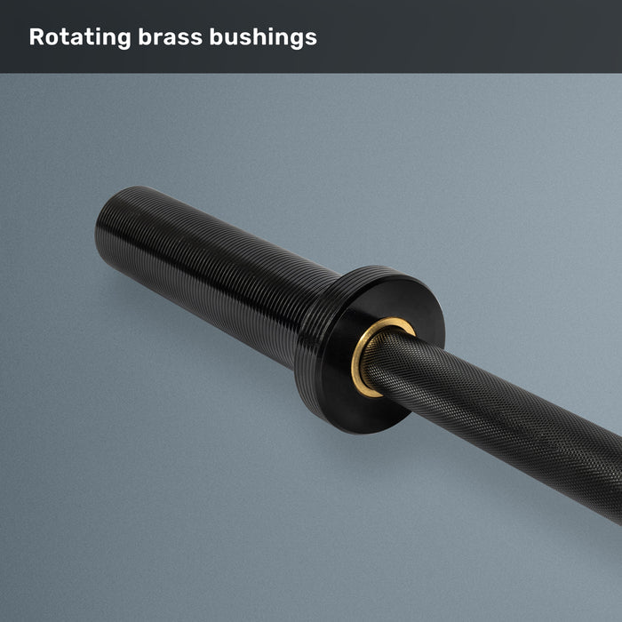 A close-up of the Bells of Steel Short Rackable Barbell in black shows its textured grip and a brass bushing near the sleeve against a gray background. The text above reads, “Rotating brass bushings.” Ideal for a compact home gym, this 69-inch barbell delivers both performance and space-saving versatility.