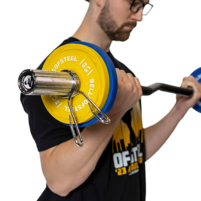 A person with glasses and a black shirt performs a bicep curl using an Olympic barbell. The polished chrome sleeves gleam as the blue and yellow plates are secured by Bells of Steel Spring Collars, standing out against the plain white background.