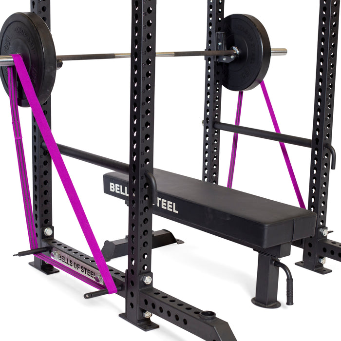 The Bells of Steel Standard Band Pegs support two purple resistance bands on a weight bench and power rack setup, adding extra resistance to the loaded barbell during bench presses.