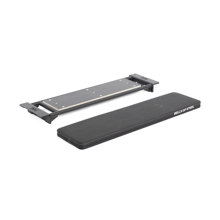 Two fitness equipment pieces on a white background: a black padded adjustable bench with "Bells of Steel" branding, and the Bells of Steel Utility Seat for Hydra/Manticore—a rectangular metal platform with textured surface and end brackets.