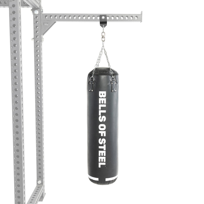 A heavy black punching bag hangs from a metal frame using the Bells of Steel Utility Shackle Rack Attachment by chains, highlighting reliable gym equipment mounting against a plain white background.