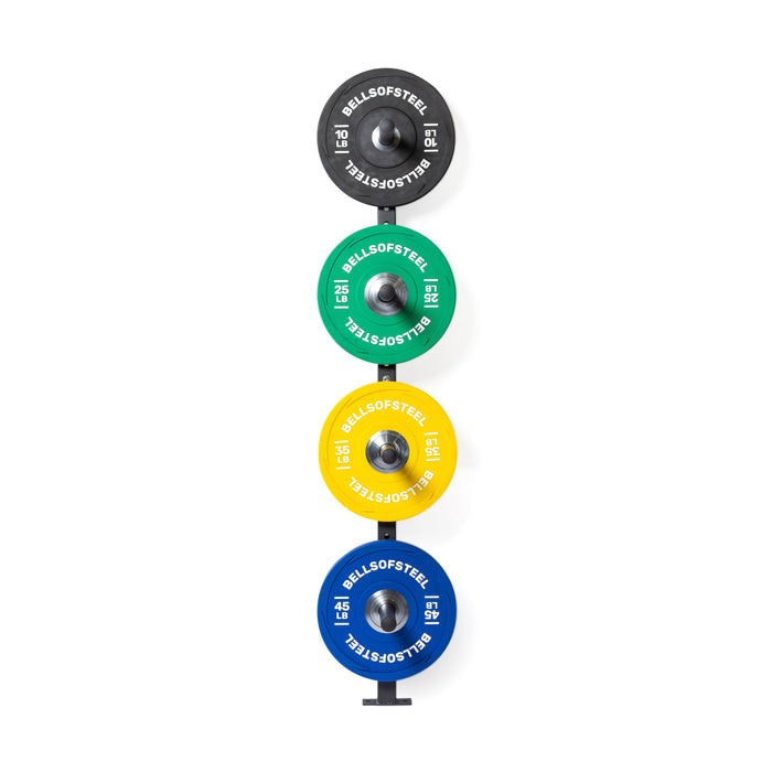 Overhead view of four colorful Bells of Steel weight plates (black, green, yellow, blue), each marked in kilograms, stacked on a Wall-Mounted Plate Storage Rack.